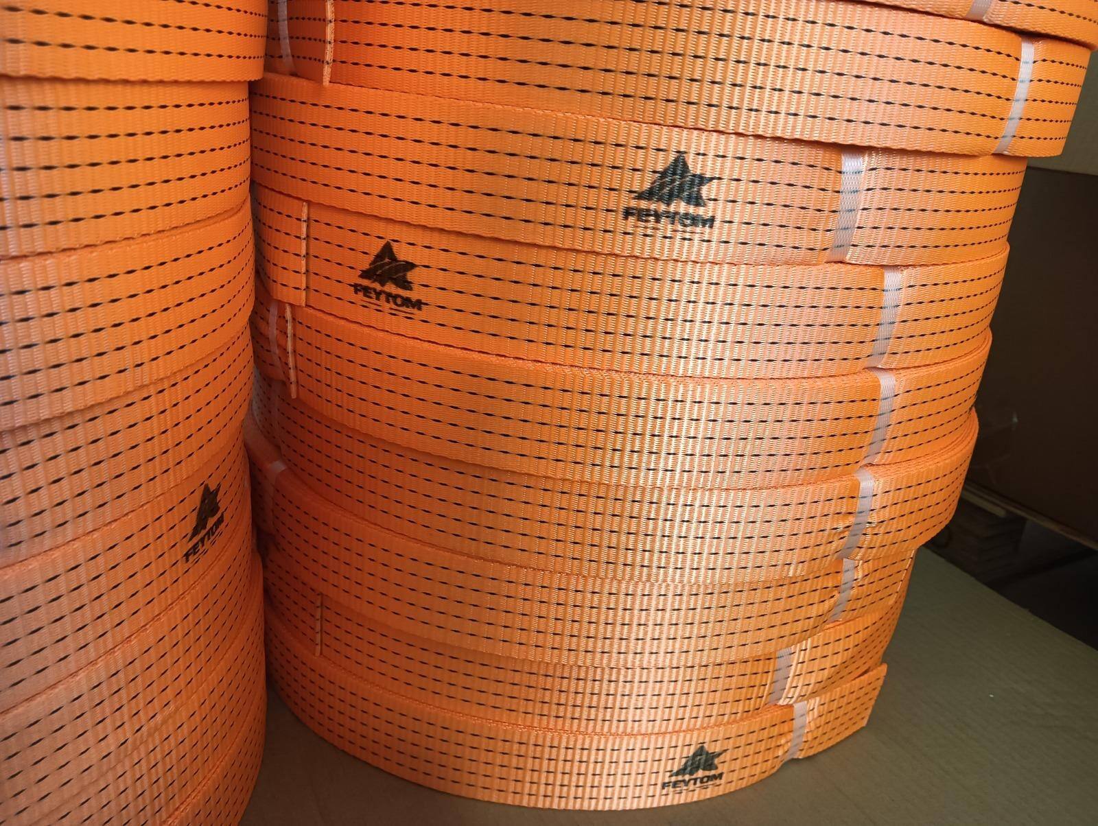 Coils of orange Feytom cargo-lashing webbing stacked on their sides. The Feytom name and mark are printed in black along the webbing, alongside the black dashed lines woven into the weave.