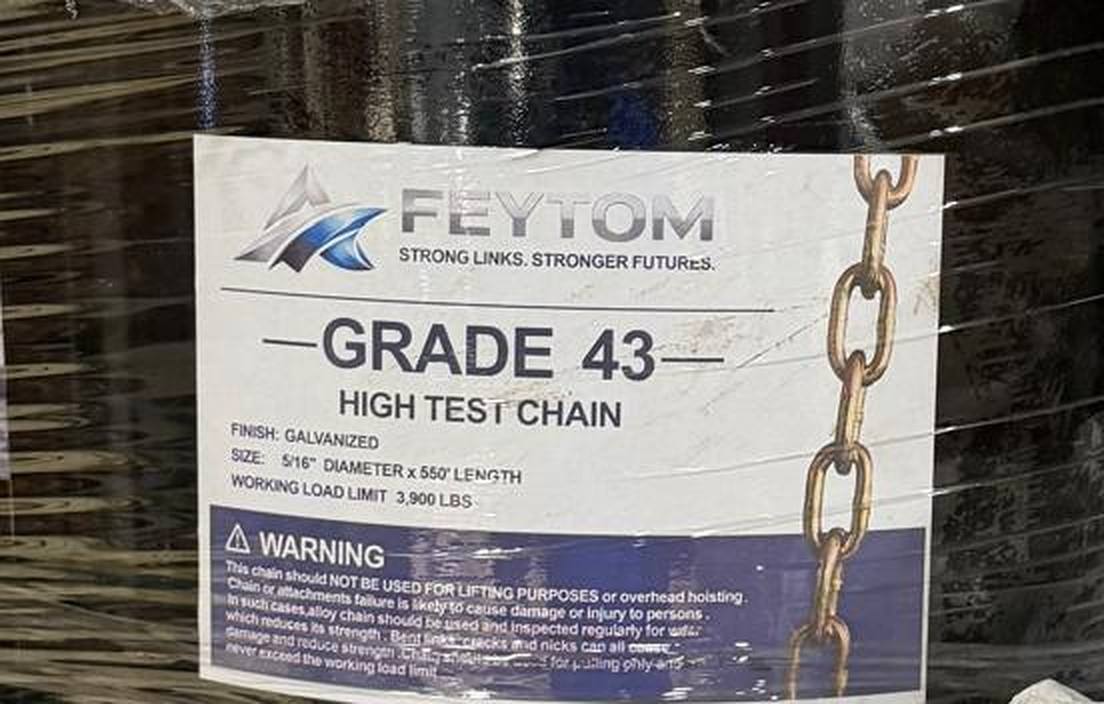 Close view of the printed label: Feytom, Grade 43 High Test Chain, finish galvanized, size 5/16 inch diameter by 550 feet length, working load limit 3,900 lbs, above a blue warning panel.